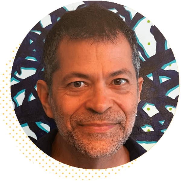 Pooch Cafe creator Paul Gilligan in a circular headshot, smiling slightly in front of an abstract black, white, and blue background with a yellow dotted accent along the lower left edge.